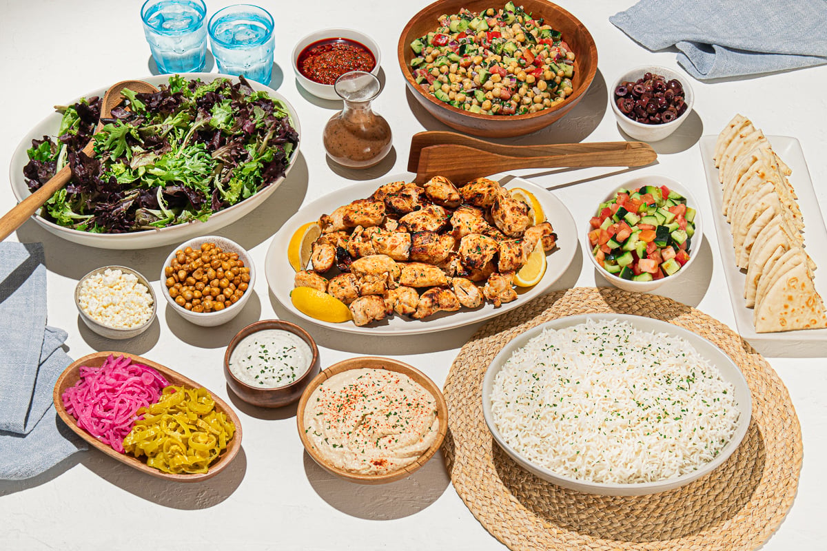 Holiday catering spread with grilled chicken, rice, salad, hummus and pita